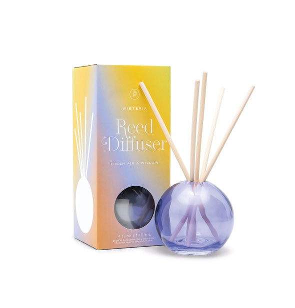 Round purple glass jar with five wooden reeds emerging from it next to Paddywax box packaging