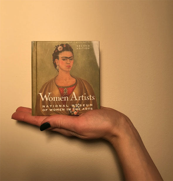 Model's hand holds the Women Artists book for size reference