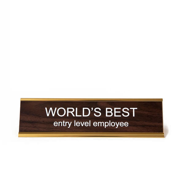 Rectangular faux wood and gold desk placard says, "World's best entry level employee" in white lettering