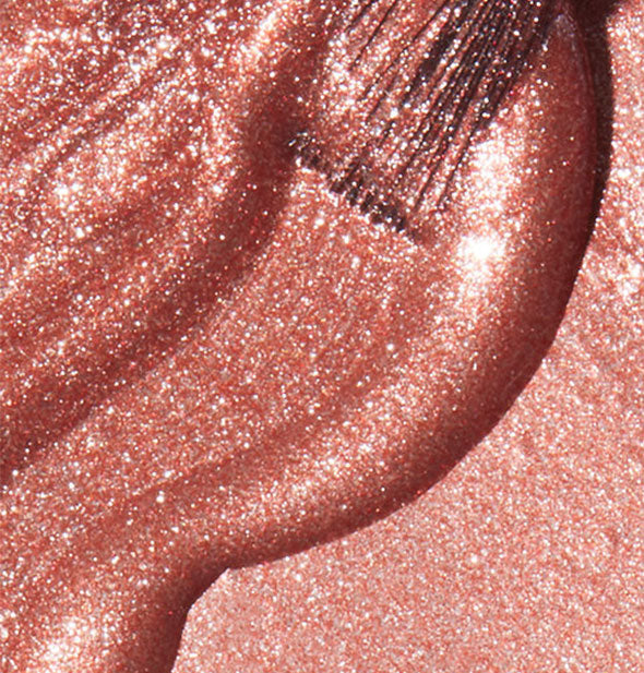 Shimmering rosy-copper nail polish with brush tip dipped into it