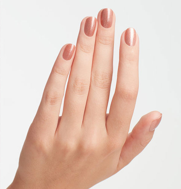 Model's hand wears a shimmery, coppery-pink shade of nail polish