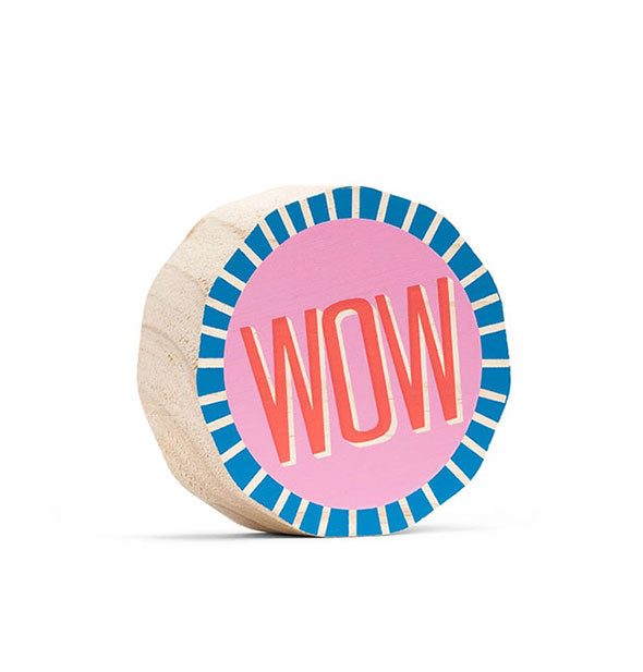 Round free-standing wooden sign painted in blue, pink and yellow with "WOW" printed in the middle