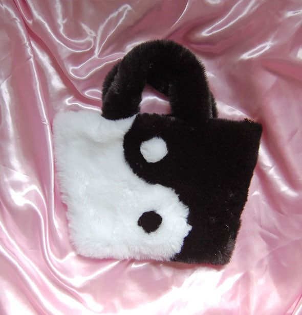 Fuzzy black and white yin yang design purse resting on pink satin fabric