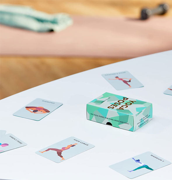 Yoga Poses cards and box on a white tabletop with yoga mat on floor in the background
