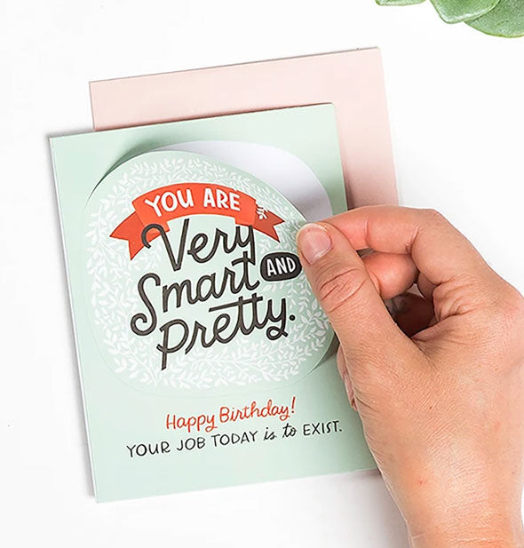 Model's hand peels back a sticker on the front of the You Are Very Smart and Pretty birthday greeting card