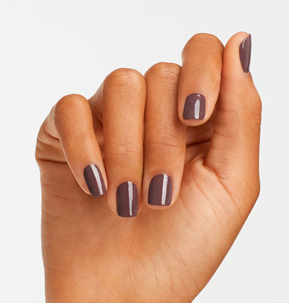Model's hand wears a purplish brown shade of nail polish