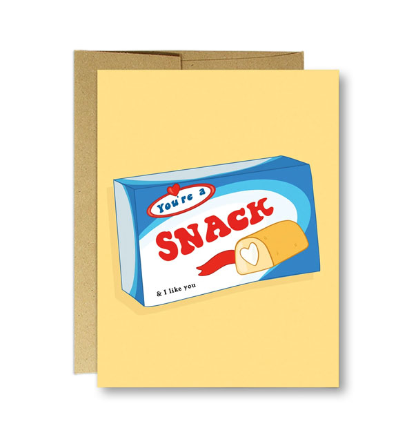 Yellow greeting card with kraft envelope behind features an illustration resembling a Hostess Twinkies box says, "You're a snack & I like you"