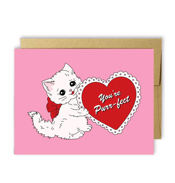 Pink greeting card with kraft envelope features illustration of a white kitten wearing a red bow and holding a lacy red heart that says, "You're Purr-fect"