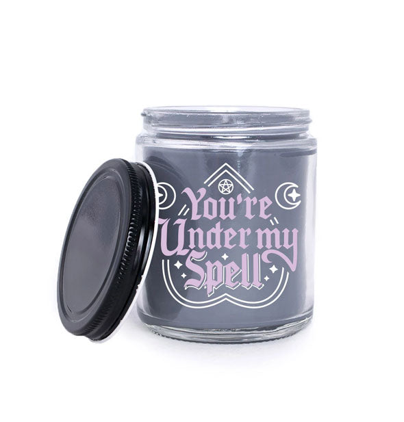 Dark wax candle in clear glass jar with black lid says, "You're Under My Spell" with white design accents