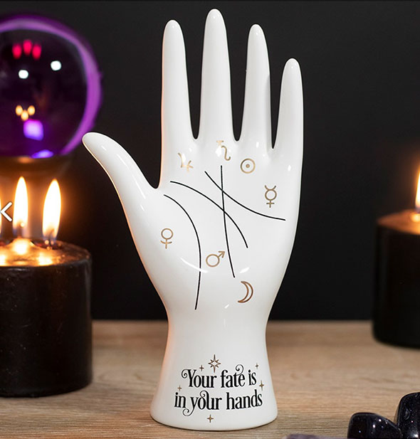White palmistry hand figurine on a wooden tabletop with lit candles and a black light