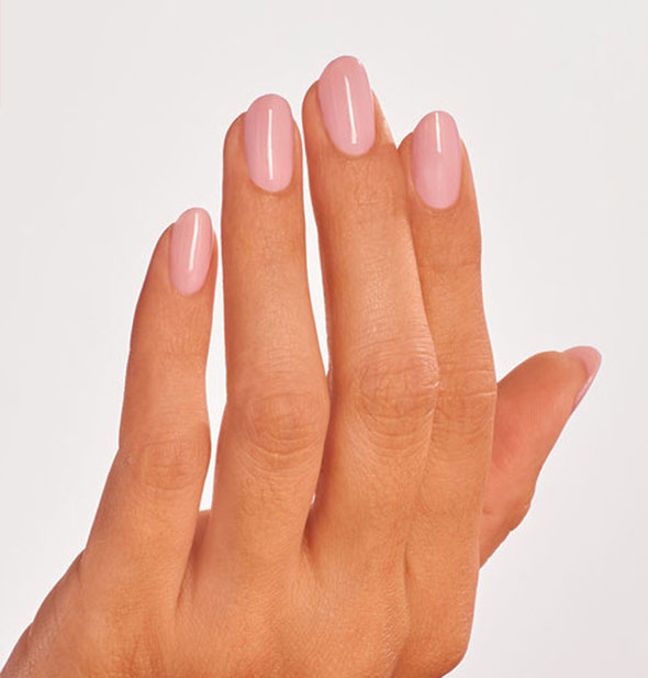 Model's hand wears a soft, neutral shade of pink nail polish