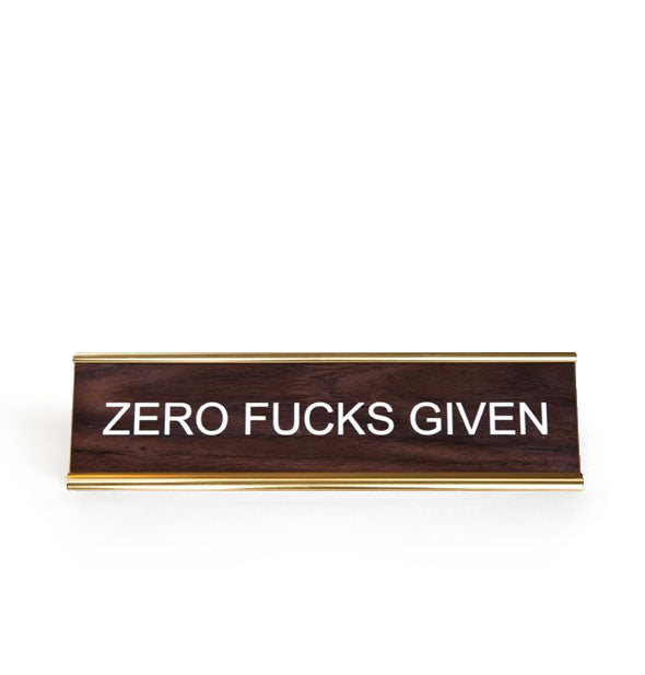 Rectangular faux wood and gold desk placard says, "Zero fucks given" in white lettering