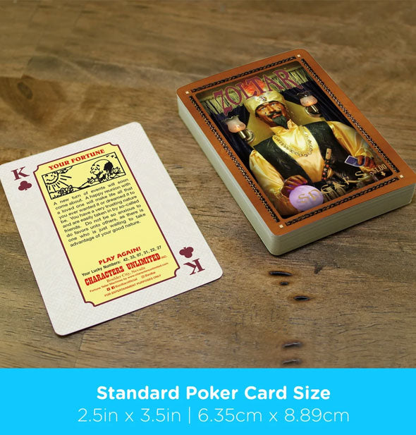 Zoltar Speaks playing card deck and king of clubs on wooden surface are labeled, "Standard Poker Card Size" with dimensions in inches and centimeters